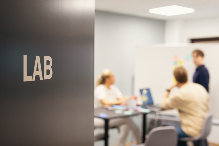 Bildet viser mennesker som arbeider på en PC på et møterom, på døren inn til rommet står det LAB