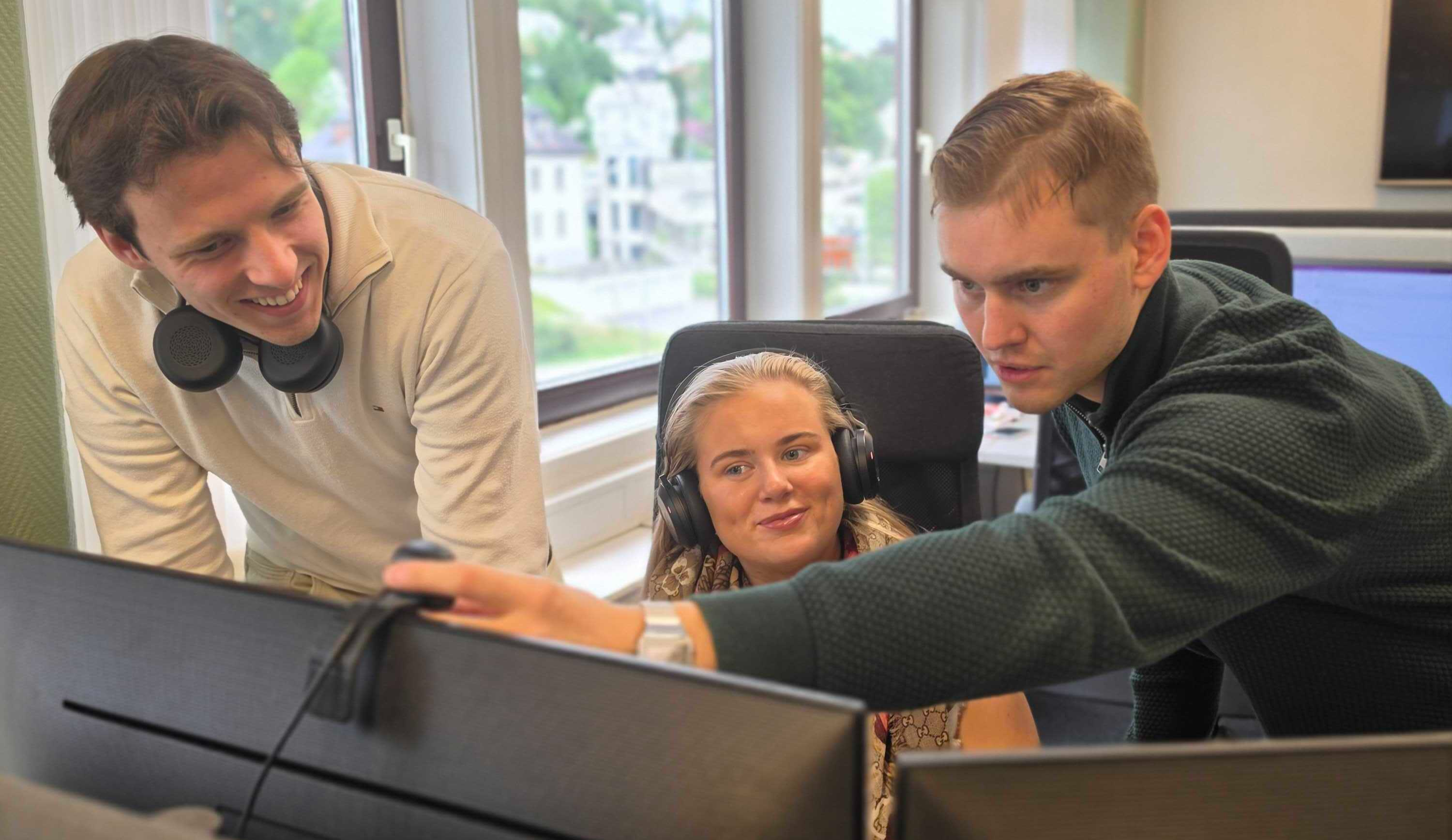 tre personer som jobber sammen foran en PC skjerm på et kontor. 